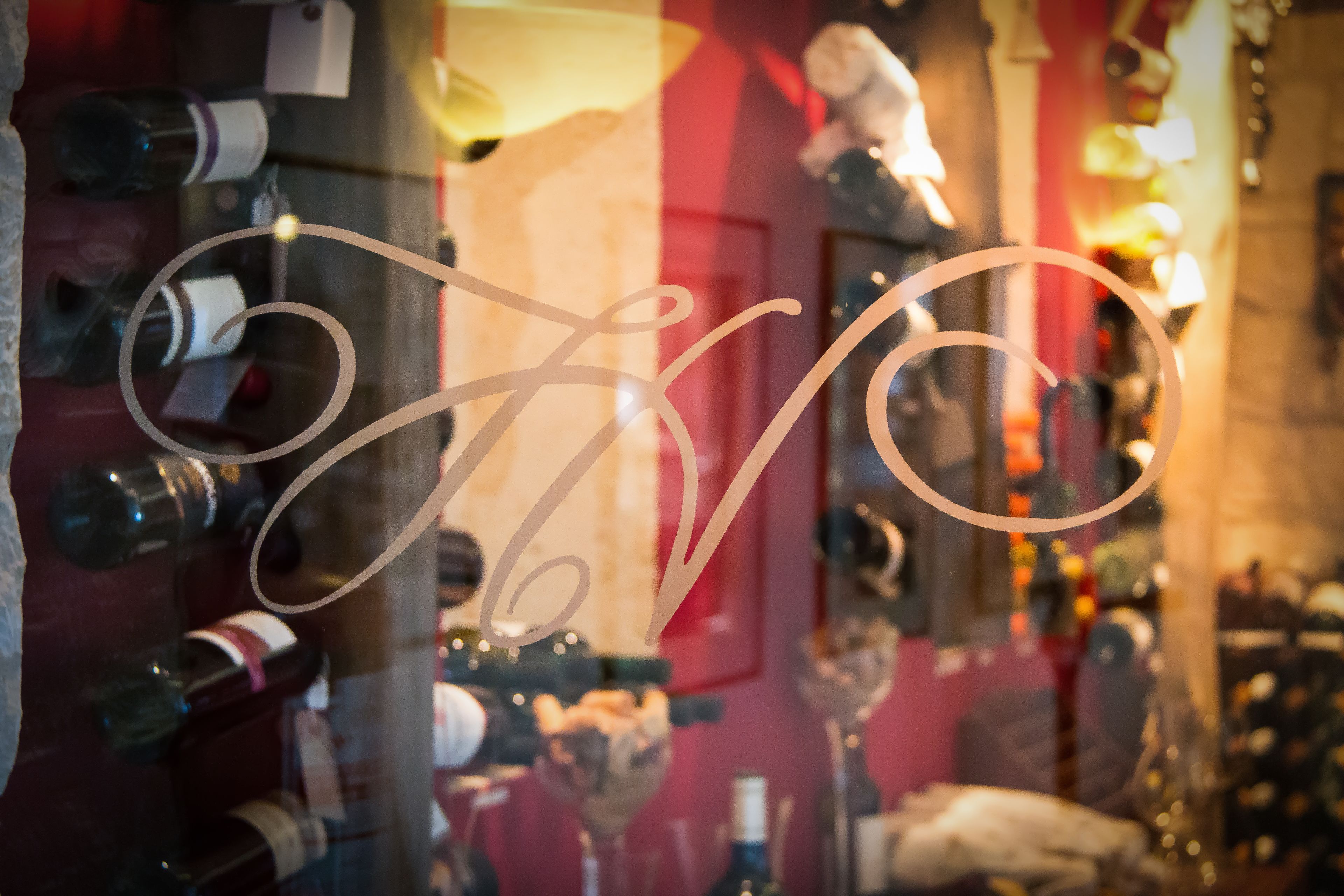 A wine rack with bottles, a glass of wine, and a decorative sign with a cursive design.