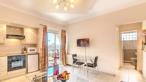 A modern kitchen with a microwave, oven, and refrigerator. There is a dining area with a glass table and chairs. A glass coffee table with fruit is in the center. - Hill View Restaurant & Apartments (Pissouri)