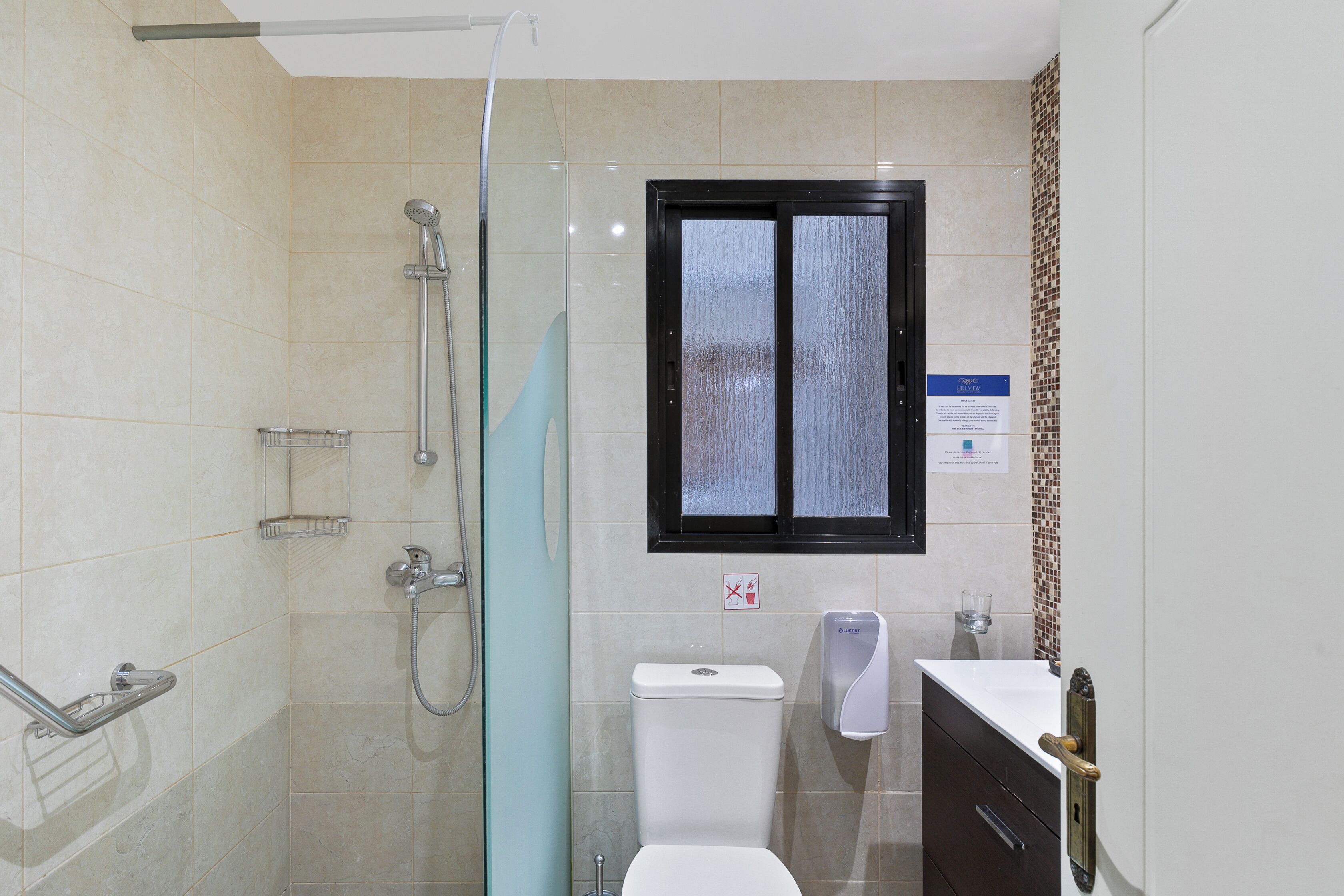 Ein modernes Badezimmer mit Duschkabine aus Glas, Toilette, Waschbecken mit Seifenspender und Fenster mit Milchglas.