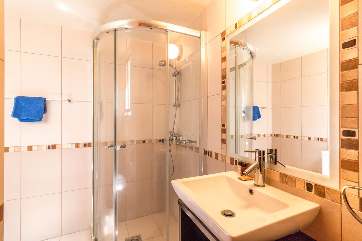 A bathroom with a glass shower enclosure, a sink, and a mirror.