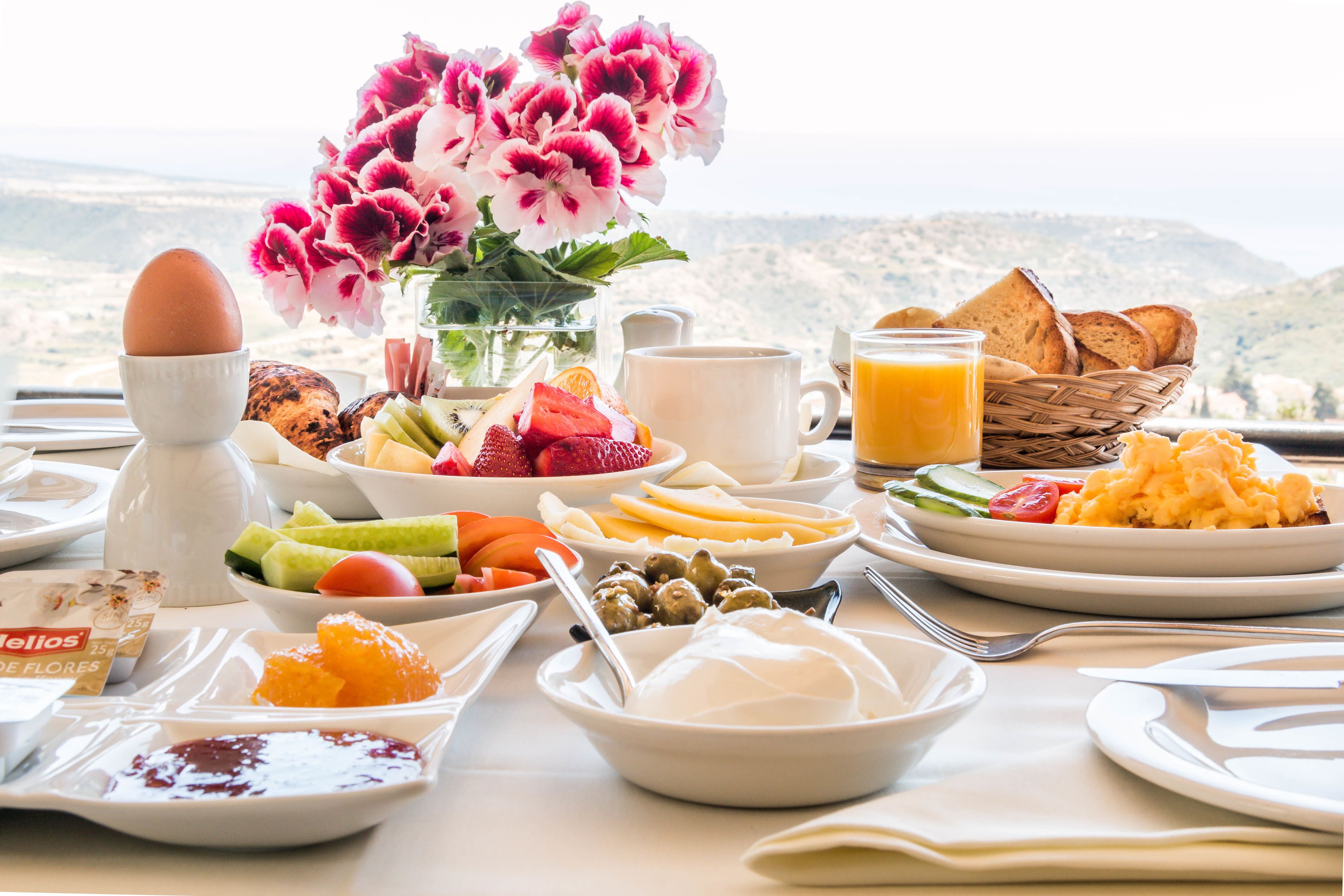 A breakfast table with a variety of foods, a vase of flowers, and a scenic view.