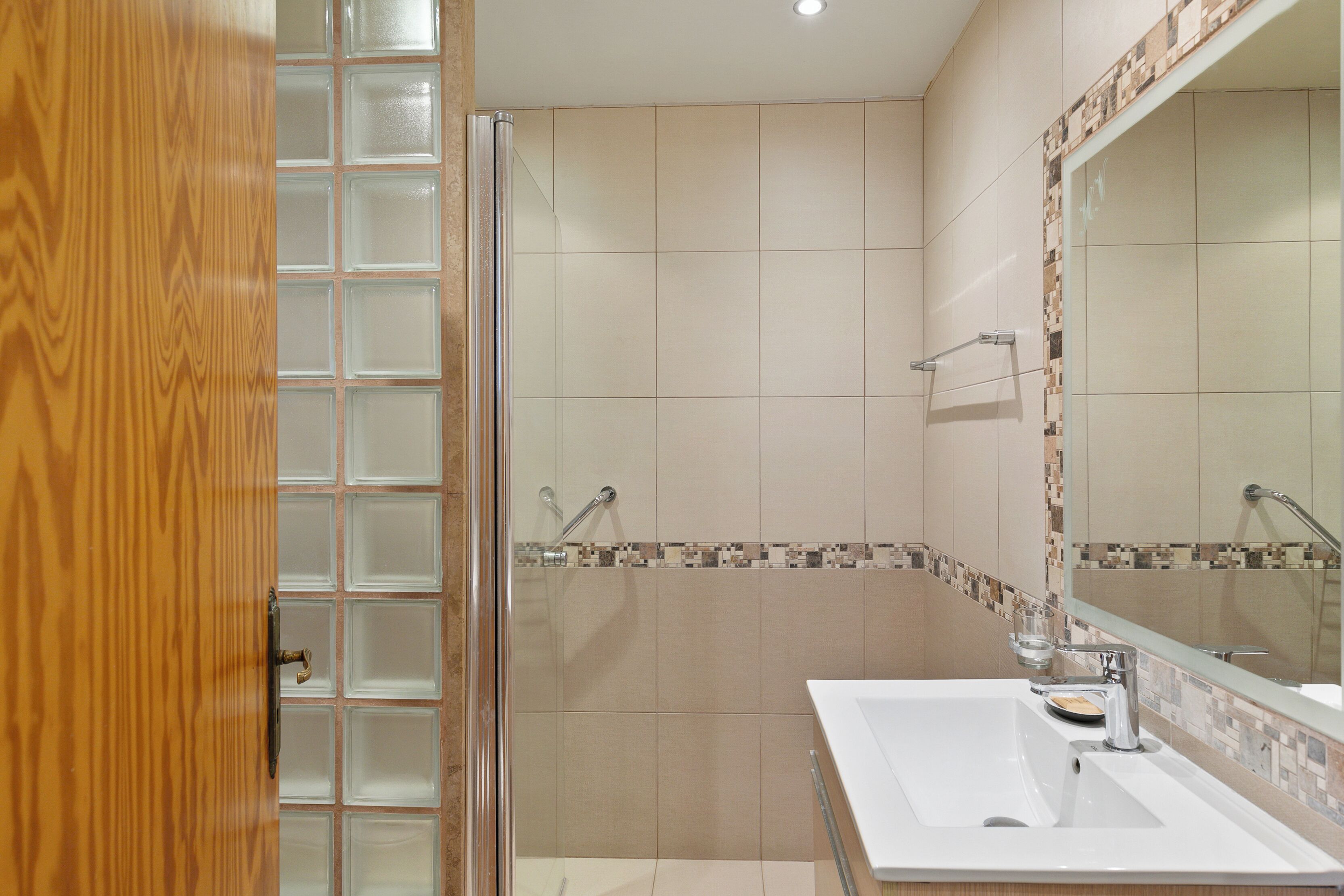 A bathroom with a glass shower enclosure, a white sink, and a mirror with a tiled backsplash.