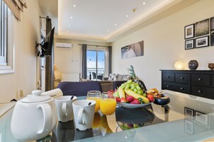 Una habitación de hotel moderna con zona de comedor y una mesa con opciones para el desayuno, incluyendo tetera, tazas y frutero.