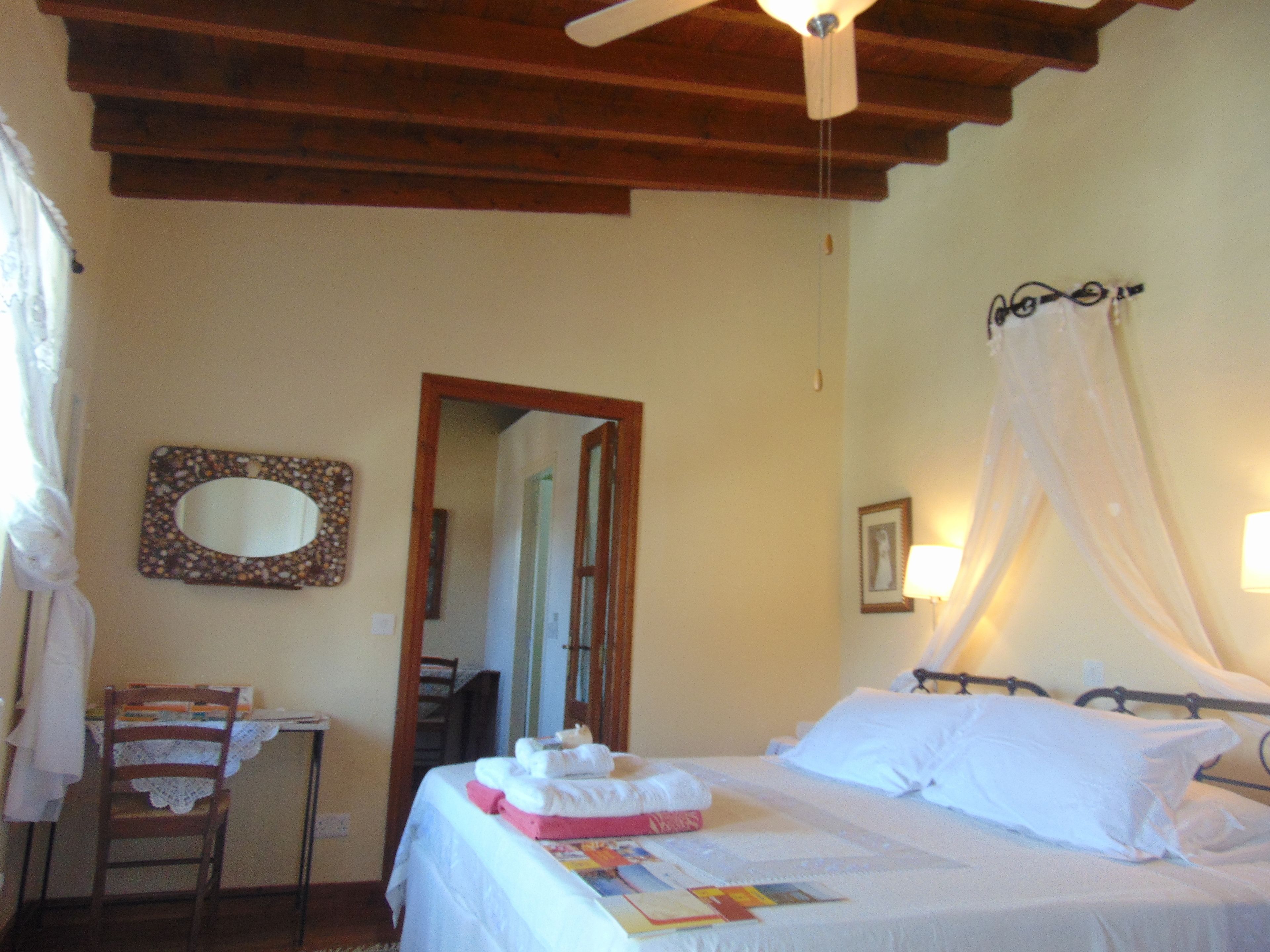 A bedroom with a bed, a bedside table, a chair, a mirror, and a ceiling fan.