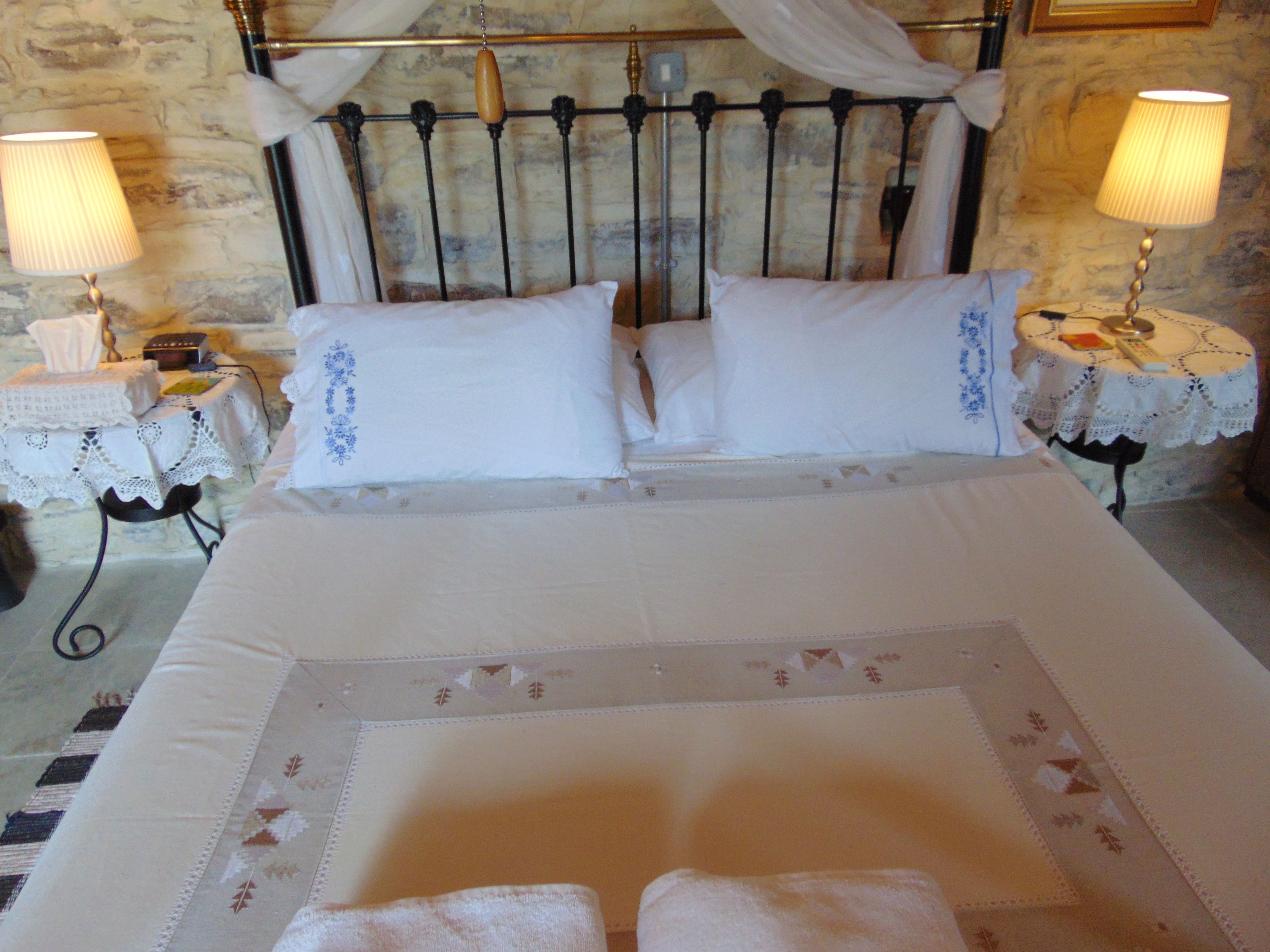A neatly made bed with white linens and pillows, two bedside tables with lamps, and a stone wall in the background.