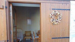 Een houten deur met een krans, een stoel, een tafel en een gestreept vloerkleed in een kamer.