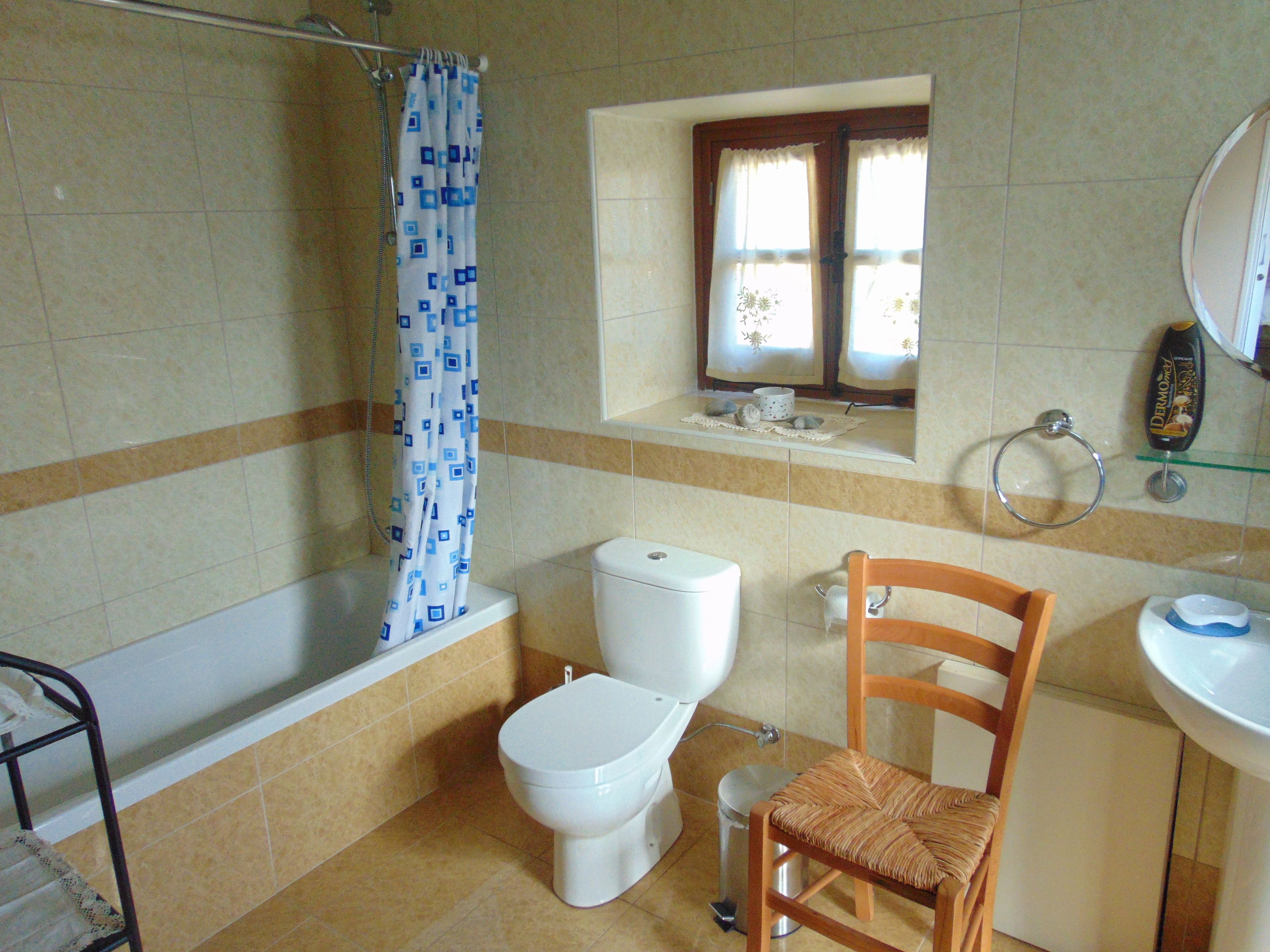 Un baño con bañera, inodoro y una silla de madera.