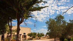 Une cour avec un bâtiment en pierre, des arbres et un ciel dégagé.
