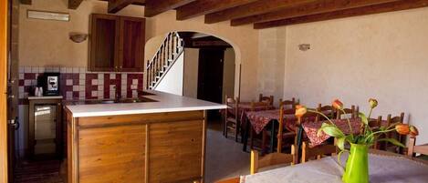 Una cocina rústica con armarios de madera, salpicadero de azulejos y un comedor con mesa preparada para cuatro.