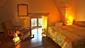 Une pièce chaleureuse avec un bureau en bois, un lit recouvert d’une courtepointe, une table de chevet avec une lampe et une fenêtre avec des rideaux.