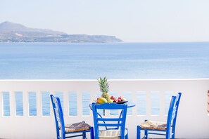A balcony with two blue chairs and a table with fruit, overlooking a calm sea and distant hills. - Kalyves Bay (Apokoronas)