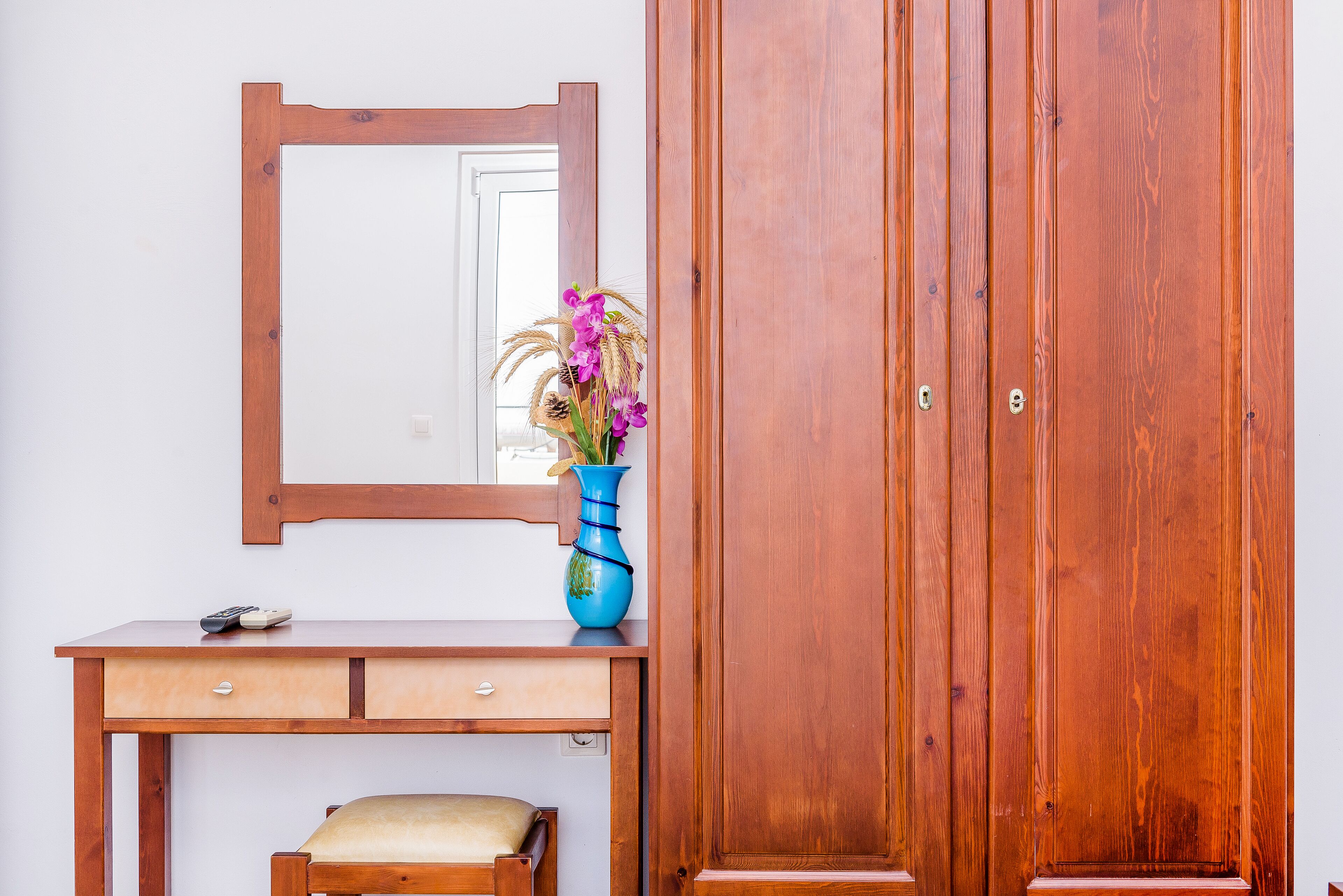 A wooden desk with a vase of flowers, a mirror, and a wardrobe.