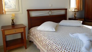 A neatly made bed with a patterned bedspread, a bedside table with a vase, and a window with curtains. - Kalyves Bay (Apokoronas)