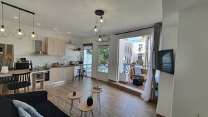 A modern kitchen with wooden cabinets, a dining area with a black sofa, and a balcony with a TV. - Elizabeth Suites (Chania)
