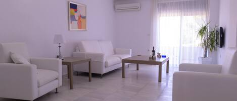 A modern living room with white furniture, a painting on the wall, and an air conditioning unit.