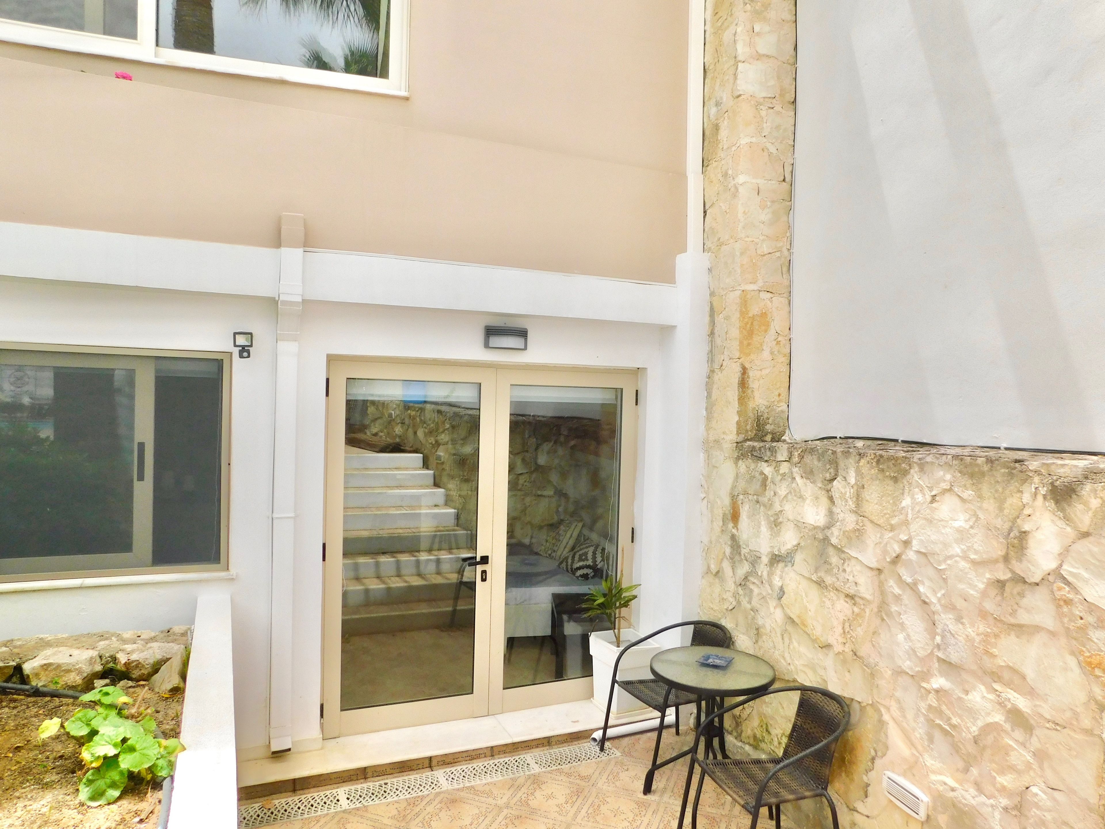 Un espace patio avec une porte vitrée donnant sur un escalier, une petite table ronde avec des chaises et une plante en pot.