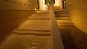A well-lit indoor staircase leading to a bright entrance area with a potted plant. - Elizabeth Suites (Chania)