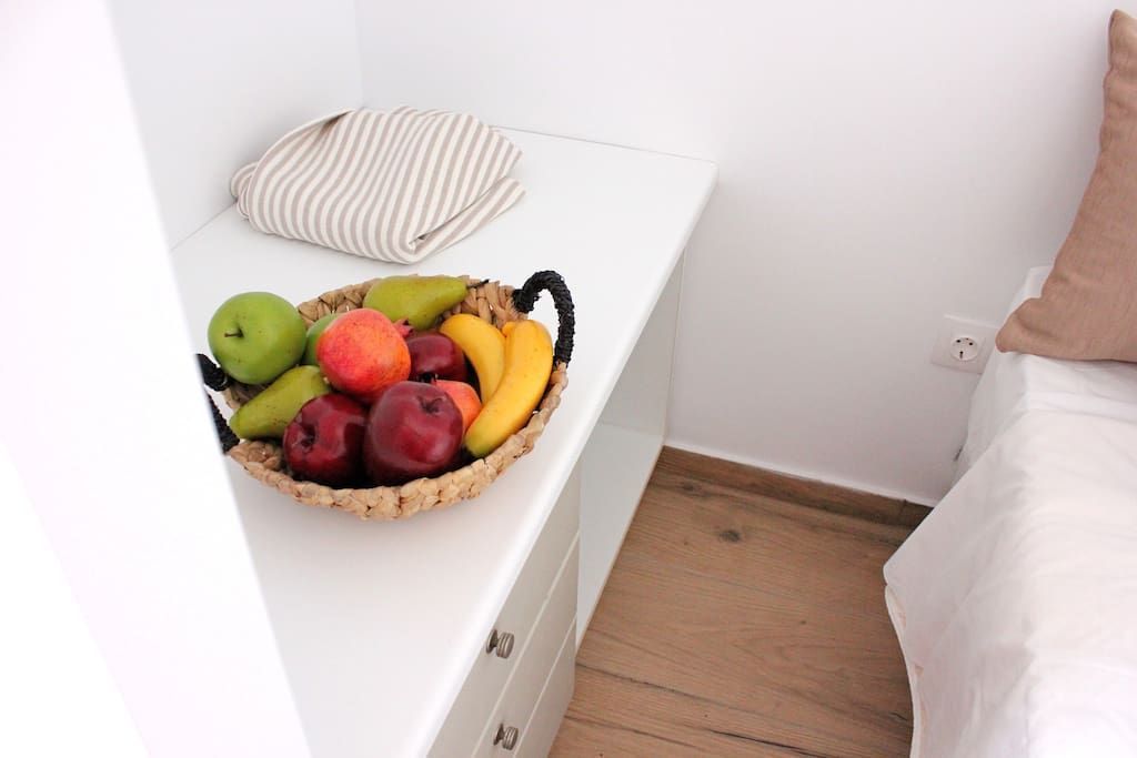 A white bedside table with a wicker basket containing various fruits.
