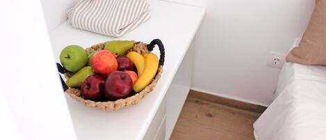 A white bedside table with a wicker basket containing various fruits.