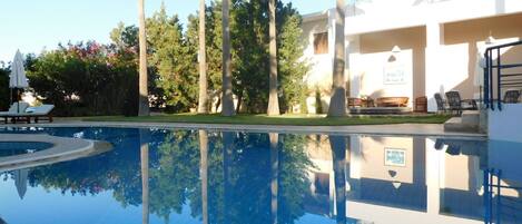 A swimming pool with clear water reflecting trees and a building.