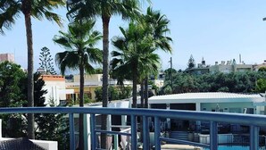 A balcony with a table and chairs, overlooking a swimming pool and palm trees. - Elizabeth Suites (Chania)