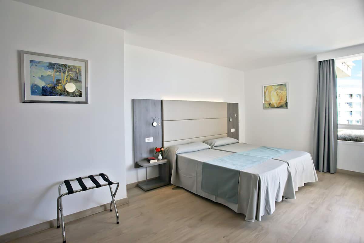 Ein modernes Hotelzimmer mit einem großen Bett, Nachttischen, einer kleinen Bank und Kunstwerken an den Wänden.
