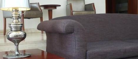 Ett vardagsrum med en grå soffa, ett bord med en lampa, en tavla på väggen och en dörr som leder till ett annat rum.