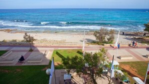 A coastal view with a sandy beach, a grassy area with benches, and a flagpole. - Aparthotel Playa Dorada (Sant Llorenc des Cardassar)