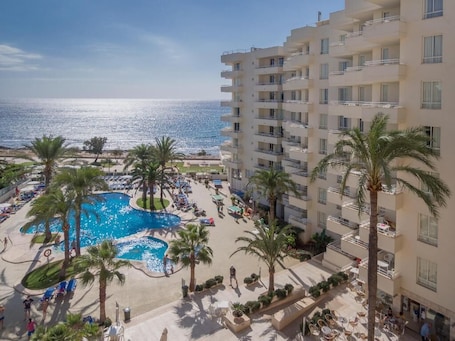 A hotel with a pool area, palm trees, and a view of the ocean.