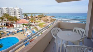 A balcony with a view of a swimming pool and beach, white chairs, and a clear sky. - Aparthotel Playa Dorada (Sant Llorenc des Cardassar)