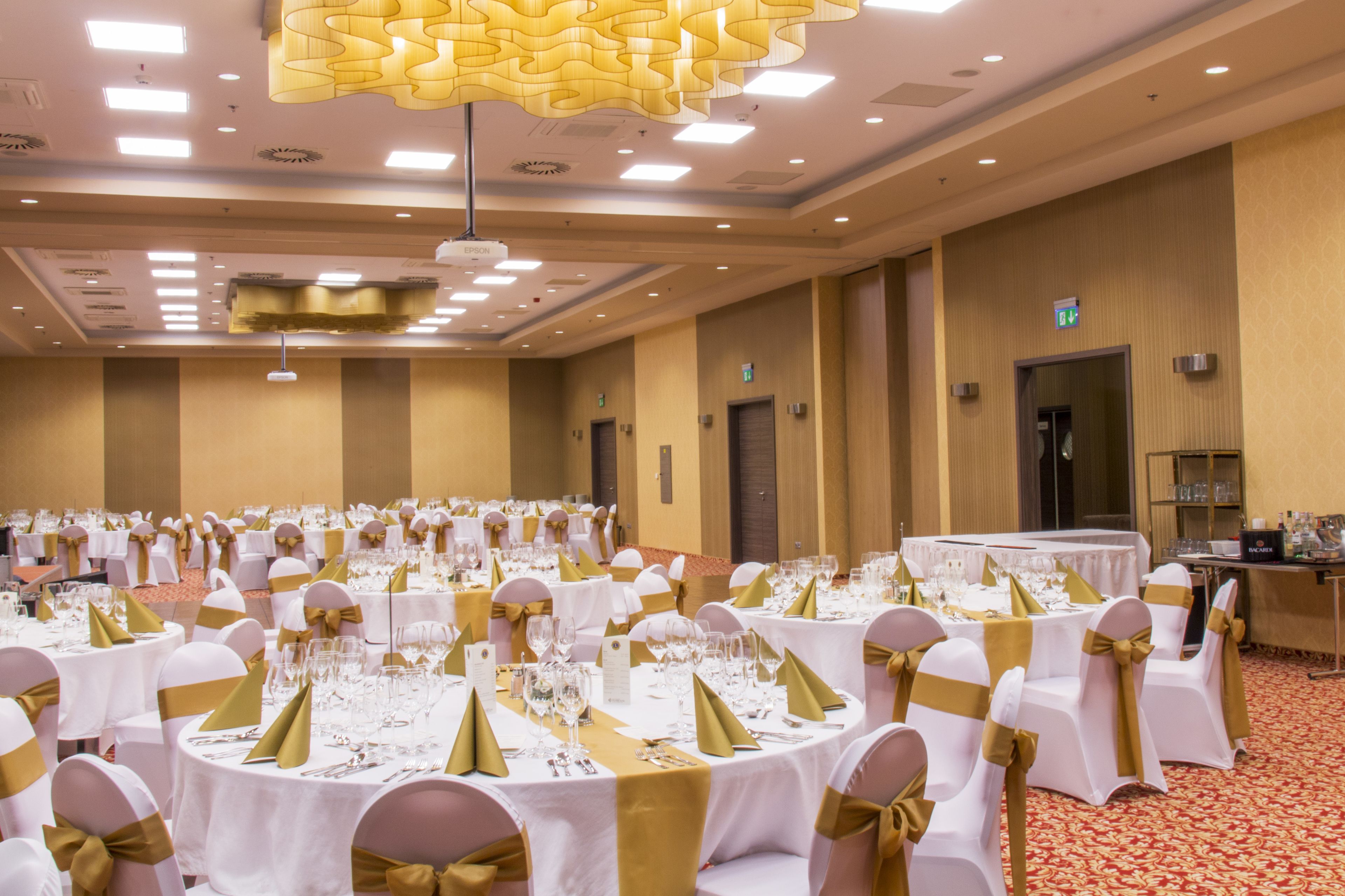 Ein Festsaal mit runden Tischen, weißen Tischdecken und goldenen Tischbändern.