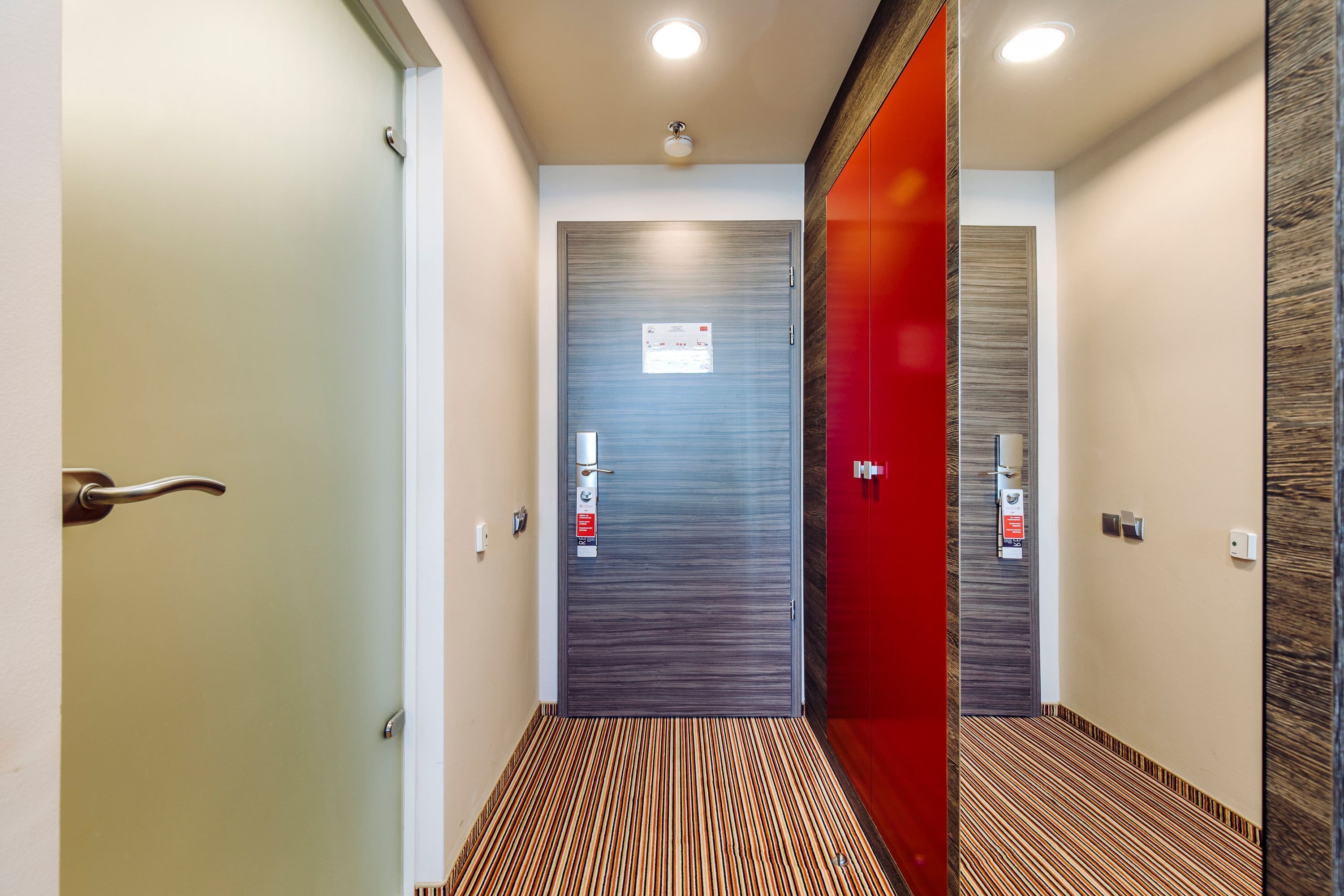 A hallway with a striped carpet, a red door, and a grey door with a fire safety sign.