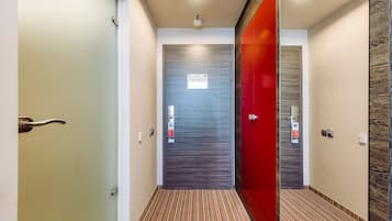 A hallway with a striped carpet, a red door, and a grey door with a fire safety sign.