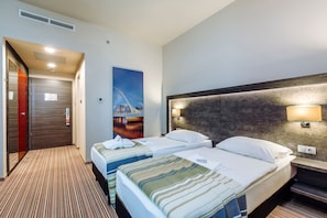 Habitación de hotel con dos camas, un cuadro en la pared, cabecera con iluminación integrada y suelo alfombrado.