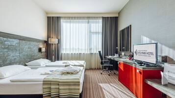 A hotel room with two beds, a desk, a television, and a view of the city through large windows.