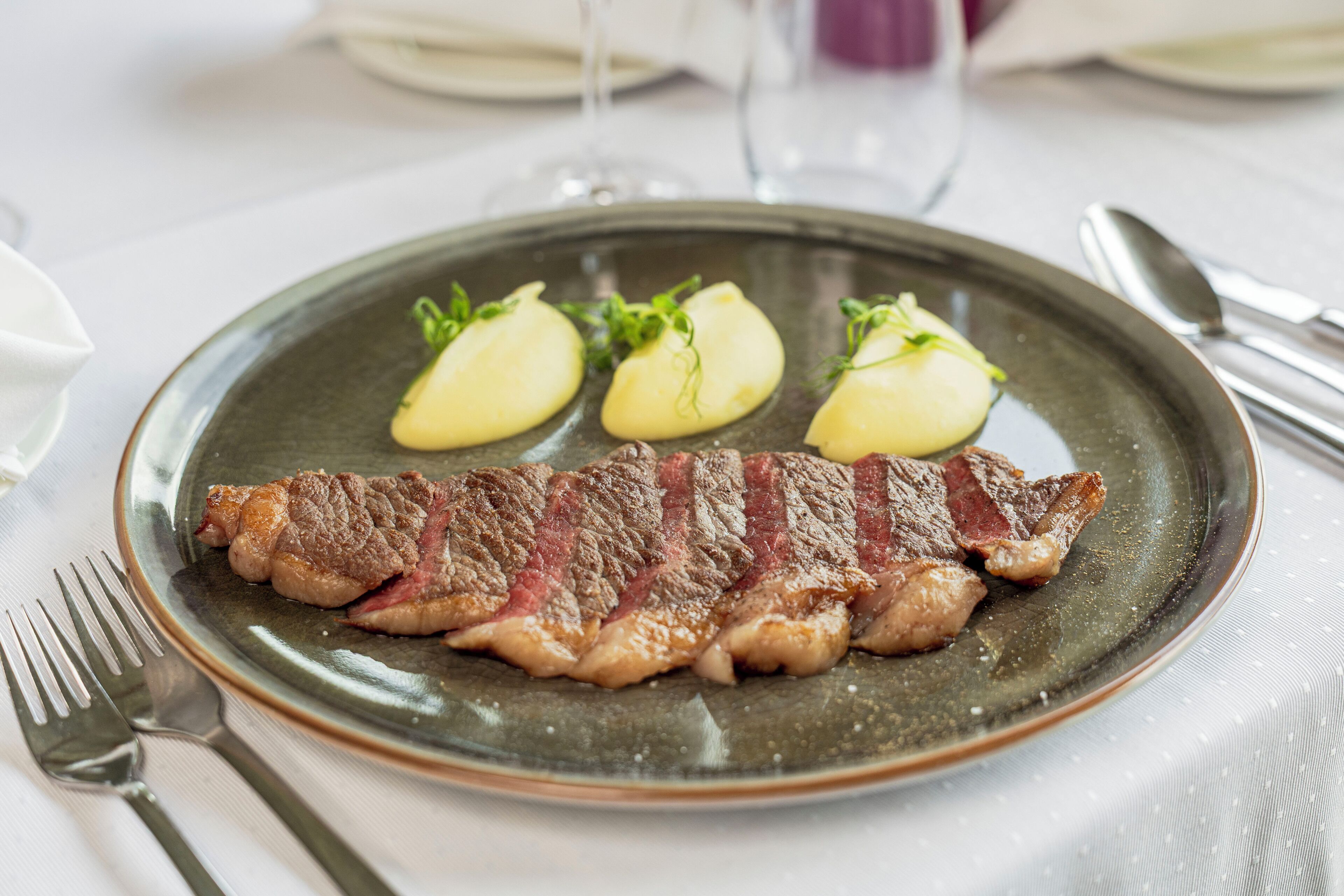 Um prato com bife e duas batatas cozidas sobre um prato de cerâmica.