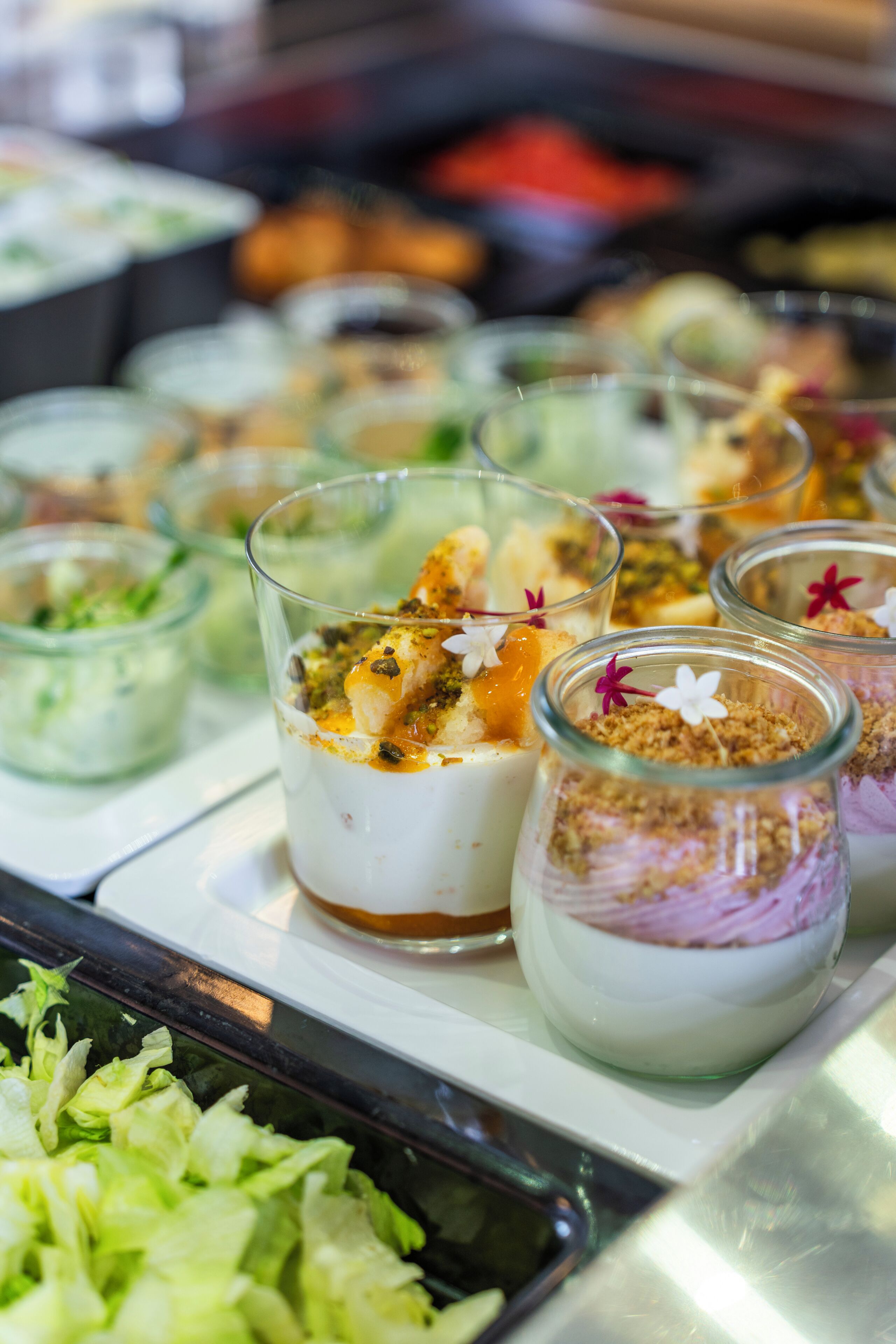 Ett urval av desserter i glasbehållare, vissa med topping och garnering, upplagda på ett fat.