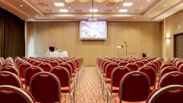 A conference room with rows of red chairs, a podium, and a projection screen.