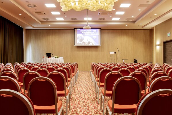 A conference room with rows of red chairs, a podium, and a projection screen.