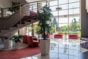 Un vestíbulo espacioso con una escalera central, asientos rojos y grandes ventanales que ofrecen vistas al exterior.