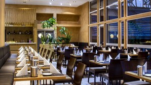 A modern restaurant with long tables, chairs, and a bar area. - ETO Park Hotel Business & Stadium (Gyor)