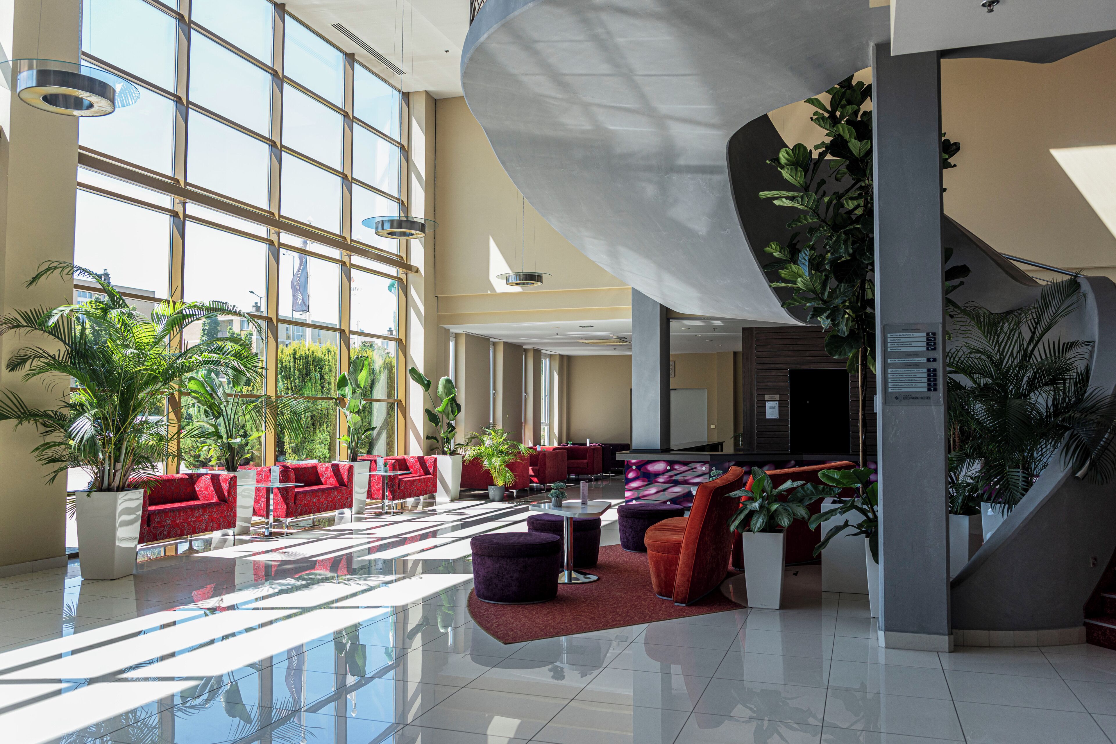 A spacious lobby with high ceilings, large windows, and a variety of seating arrangements including red sofas and purple chairs.