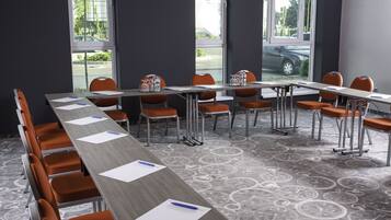 A conference room with a long table, orange chairs, and large windows with a view of the street.