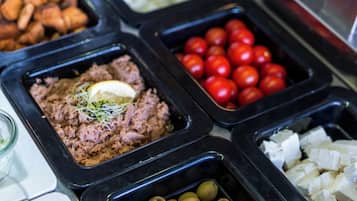 A buffet with various food options including meat, cheese, olives, and tomatoes.