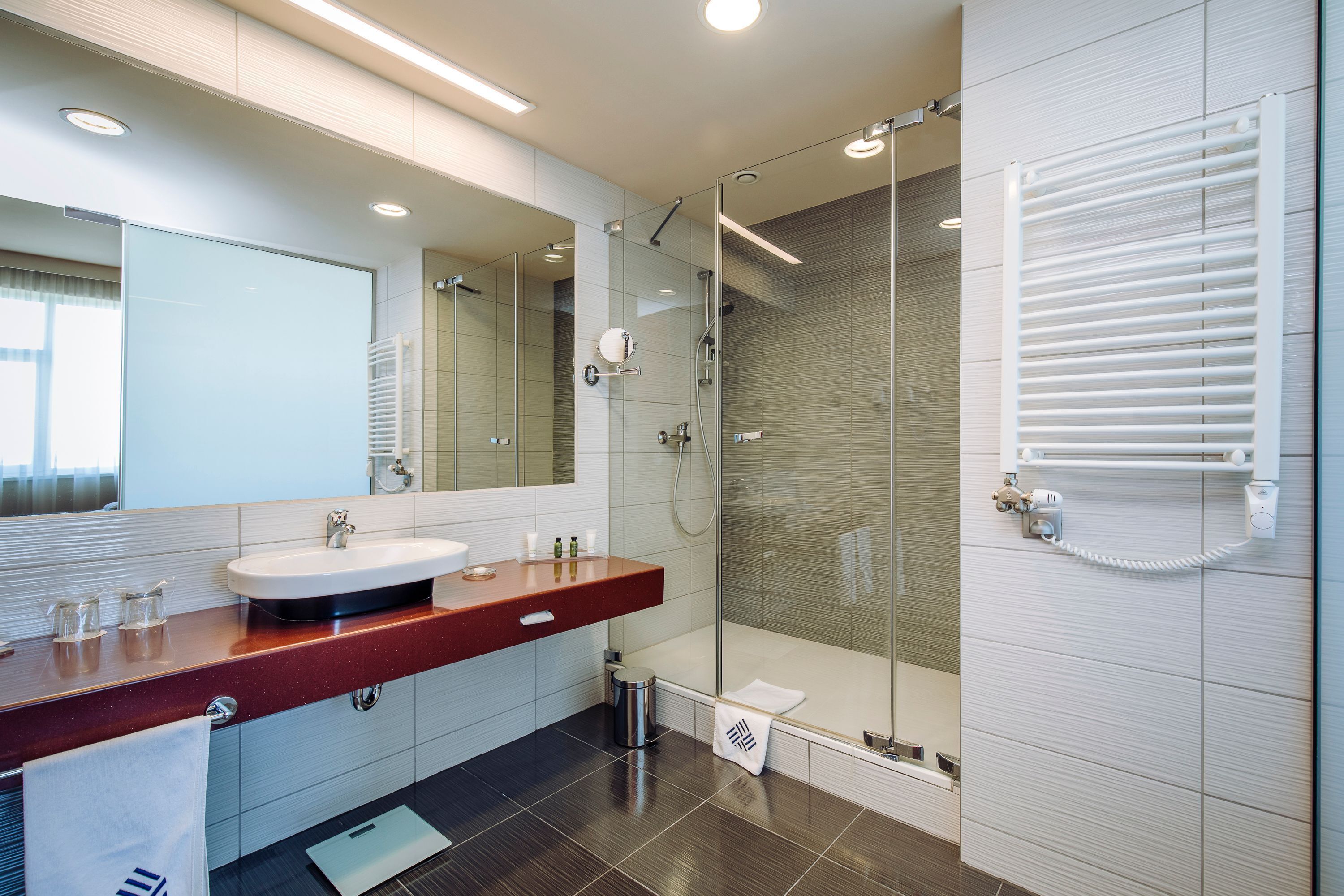A modern bathroom with a glass-enclosed shower, a large mirror, and a red countertop sink.