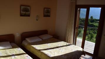 A bedroom with two beds, a balcony with a view, and two framed pictures on the wall.