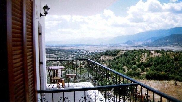 Un balcón con mesa y sillas, con vistas a un valle con árboles y montañas lejanas.