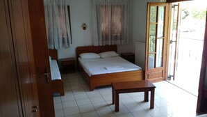 Un dormitorio con cama, mesitas de noche, un banco de madera, una lámpara y vistas al exterior a través de una puerta.