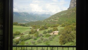 Vista desde una ventana que da a un valle verde con una montaña y un acantilado.