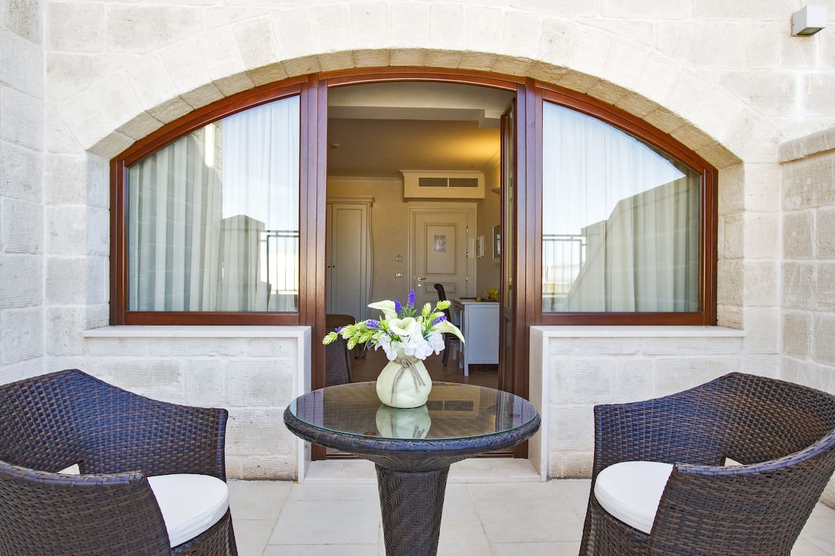 A glass-top table with two wicker chairs, a vase with flowers, and a stone wall with an arched doorway leading to a room.